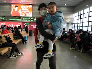 A woman carries a boy as they wait to board their train at the Beijing West Railway Station