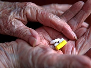 An elderly woman's hand holding prescription pills