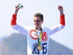 Great Britain triathlete Alistair Brownlee raises both hands in the air holding his Olympic gold medal