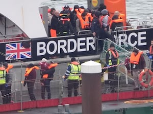 A man carries a young child as a group of people thought to be migrants are brought in to Dover