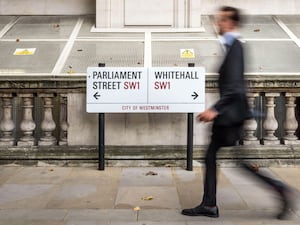 A suited office worker passing a street sign for Parliament Street and Whitehall in Westminster