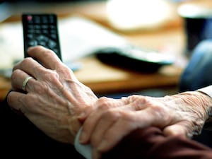 An elderly person holding a remote control in their hand