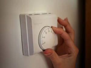 A person turning the dial on a central heating thermostat