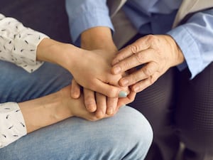 A younger person's hands holding the hands of an elderly person