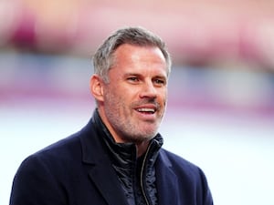 TV pundit Jamie Carragher smiles while stood on the sidelines at a stadium