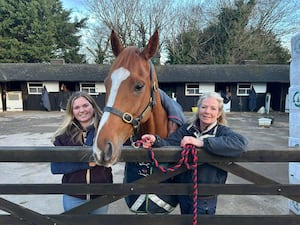 A horse with a woman on either side of it at a stables