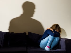 The shadow of a man with a clenched fist as a woman cowers on a sofa