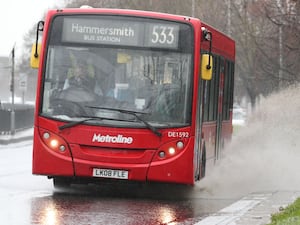 A red London bus making a splash as it drives through a puddle on the road