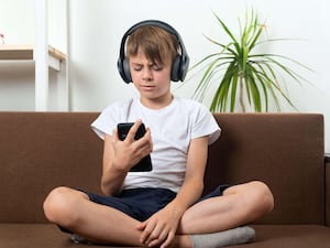 Boy on couch with headphones and phone in his hands. Child is listening to an audiobook