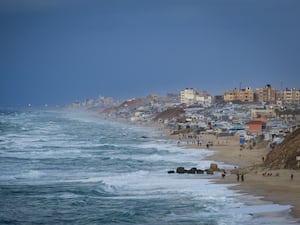 People walk along the beach next to a tent refugee camp for displaced Palestinians in Deir al-Balah