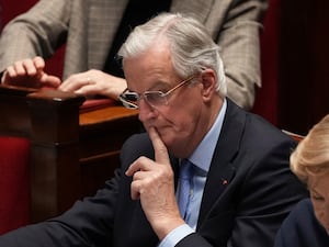 Michel Barnier holding his finger to his lips and looking concerned