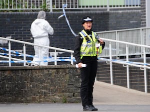 Police and a forensic investigator near police tape outside a school