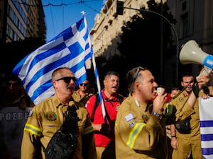 Firefighters hold a Greek flag as they march during the protest in Athens