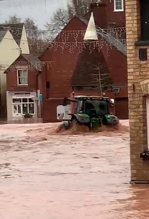 A man in a tractor driving down Tenbury Wells high street creating waves that hit shops