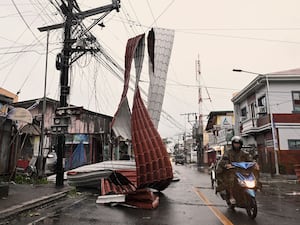 Motorists ride past a part of a roof suspended on electric wires blown by strong winds caused by Typhoon Man-yi along a street in the municipality of Baler, Aurora province, northeastern Philippines