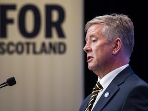 SNP depute leader Keith Brown photographed from the side speaking at a lectern, with the words 'For Scotland' on the wall behind him