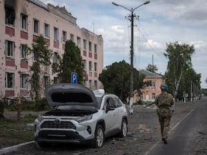 Soldier walks past a damaged car