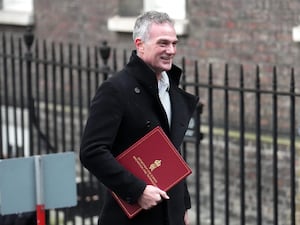 Peter Kyle walking past black railings holding a red folder