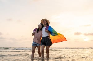 Young couple walking along beach wearing pride flag.