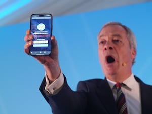 Nigel Farage holding a phone displaying the number of Reform UK party members