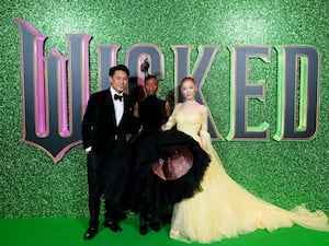 Jon M Chu, Cynthia Erivo and Ariana Grande in front of a Wicked poster