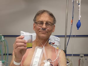 Greg Hutton in a hospital bed holding a glass of juice