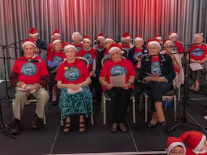 A group of elderly people dressed in red tops and Santa hats sat on chairs as they make-up the World Oldest Choir