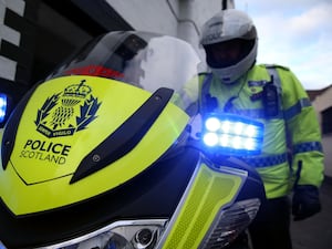 Police motorcyclist with blue lights on and Police Scotland badge prominently displayed on front of bike