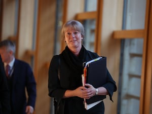 Shona Robison walking through a corridor at Holyrood, holding a black folder