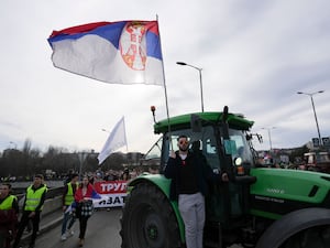 A farmer holding a Serbian flag stands on a tractor during the protest in Belgrade