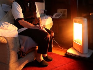 An old person sitting in front of an electric fire