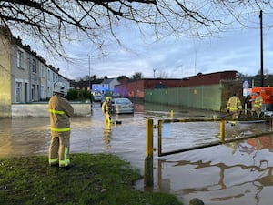 Firefighters stand on a flooded road