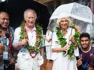 The King and Queen smile as they shelter under umbrellas while standing with members of the Apia rugby team during a visit to the Samoan Cultural Village in Apia.