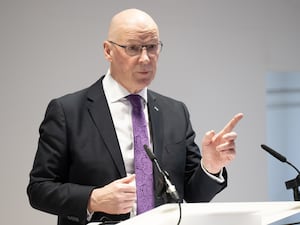 John Swinney pointing with one hand while speaking at a podium