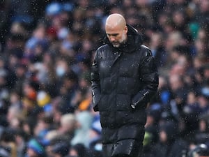 Manchester City manager Pep Guardiola, with hands in pockets, looks down on the touchline