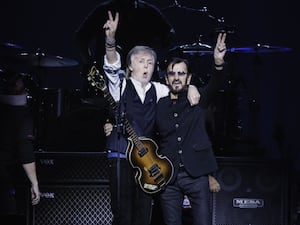 Sir Paul McCartney, left, and Sir Ringo Starr making peace signs with their hands on stage