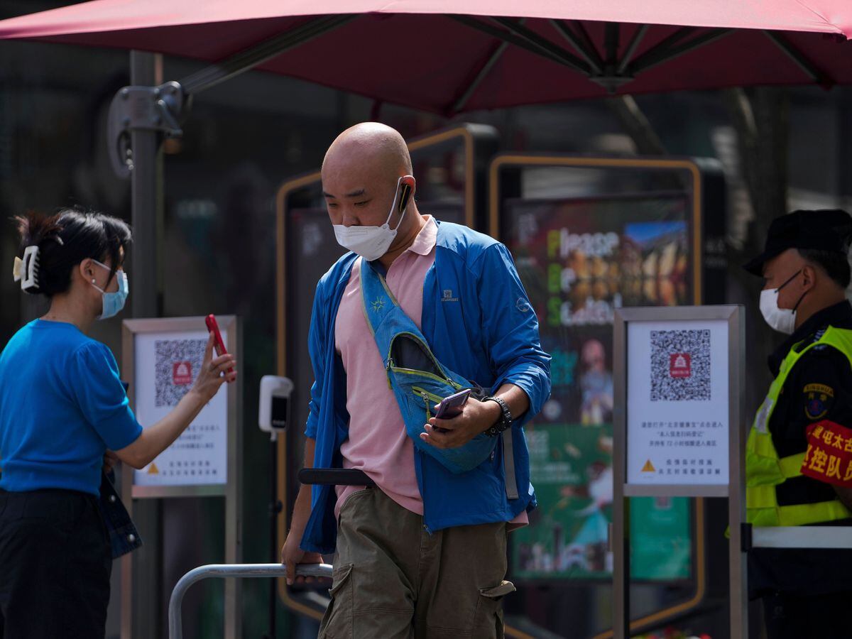 A delivery man wearing a mask walks past a masked woman and shows a security guard her health screening QR code before entering an open-air shopping mall in Beijing