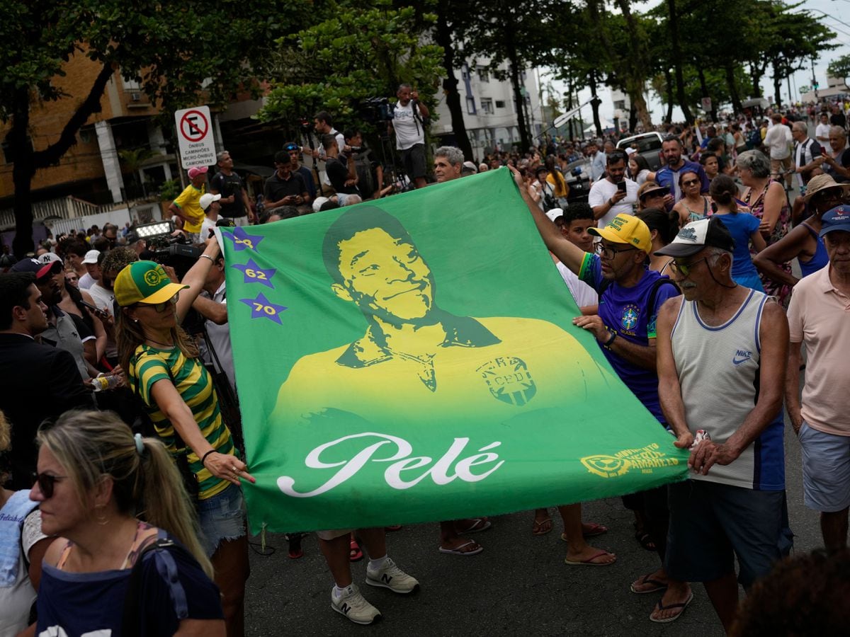 People hold a banner of the late Brazilian football great Pele along the route of his funeral procession from Vila Belmiro stadium to the cemetery in Santos, Brazil